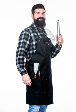 Adam mutfak aletlerini barbeküde tutuyor. Açık havada et kızartmak için aletler. Piknik ve barbekü. Parkta et pişiriyorum. Barbekü ustası. Sakallı hippi barbekü için önlük giyer. Kızartma ve ızgara yemek.