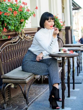 Kek tatlısıyla kafeyi rahatlatan kız. Keyifli zaman ve rahatlama. Lezzetli gurme pastası. Çekici esmer kadın, arka planda gurme kek yiyor. Mide zevki. Gurme konsepti