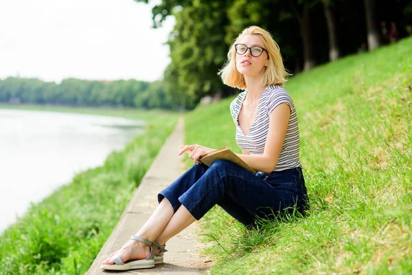 Een vrouw droomt van vakantie. Rust ontspannen en hobby. Breng vrije tijd door voor jezelf. Meisje zit op groen gras bij de rivier. Vakantie seizoen. Zomervakantie. Meisje ontspannen aan de rivier na werkdag — Stockfoto