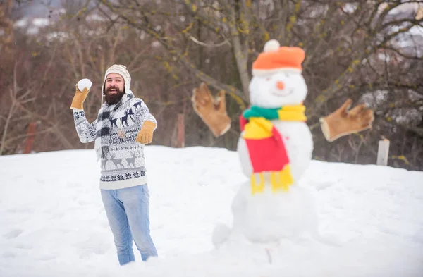 Ας χιονίσει. Χριστουγεννιάτικες διακοπές. Ενεργός τρόπος ζωής. Παιχνίδια χιονιού. Ελεύθερος χρόνος στον καθαρό αέρα. Χιονάνθρωπος και χαρούμενα γενειοφόρος hipster πλεκτό καπέλο και ζεστά γάντια παίζουν με το χιόνι σε εξωτερικούς χώρους. Καλή χειμωνιάτικη μέρα — Φωτογραφία Αρχείου