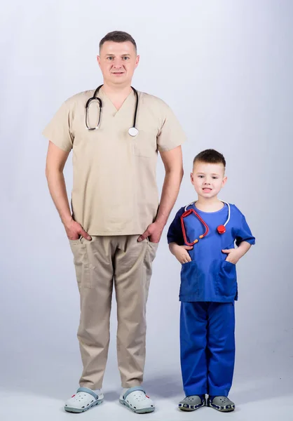 미래의 직업. 아빠로서 의사가 되고 싶어요. 귀여운 아이가 의사 놀이를 합니다. 가정 의사. 소아과 의사의 개념. 약 과 건강 관리. 청진기를 든 아버지와 작은 아들 의사 제복 — 스톡 사진