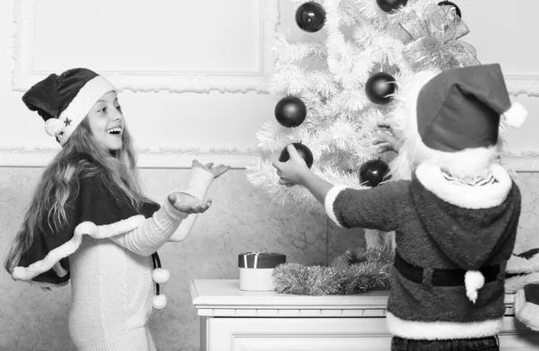 Kinderen in de santa hoeden versieren kerstboom. Familietraditie concept. Kinderen versieren kerstboom samen. Broers en zussen drukke versieren. Jongen en meisje versieren van de boom. Geliefde vakantie activiteit — Stockfoto