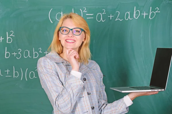 Modern laptop sörf İnternet kara tahta arka plan ile eğitimci akıllı bayan. Kadın öğretmen giyim gözlük dizüstü internette sörf tutar. Temel okul eğitimi. Dijital teknolojiler konsepti