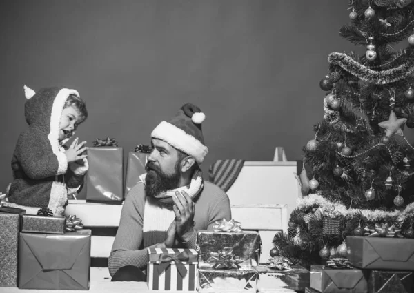 Kerstman en kleine assistent onder geschenkdozen in de buurt van kerstboom. — Stockfoto