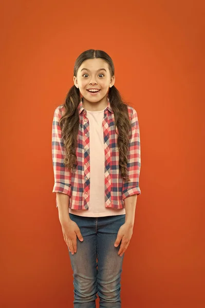 Surpreendido com boas notícias. menina laranja fundo. moda infantil. Menina da escola sorridente. Cabelo comprido. menina pequena camisa xadrez. criança surpresa. feliz dia das crianças. felicidade infantil — Fotografia de Stock