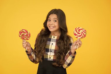 Zararlı yiyecekler. Tatlılara bayılırım. Şeker bağımlılığı. Tatlı şekerli mutlu çocuk. Elinde lolipop tutan çocuk şeker sarısı arka planda. Şekerli mutlu çocuk. Okul beslenmesi. Kalori ve enerji