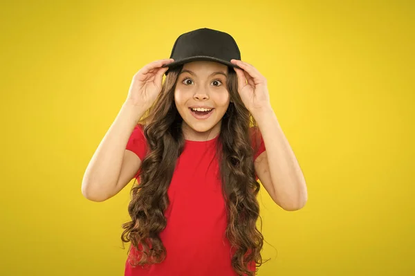 Aventura da moda. infância feliz. beleza e moda. menina pequena com cabelo comprido. menina legal com cabelo encaracolado longo. moda infantil. menina feliz na moda boné hipster. hipster criança no fundo amarelo — Fotografia de Stock