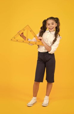 Yaparak öğreniyorum. Geometri dersinde sarı arka plan hakkında bir şeyler öğrenen tatlı küçük kız. Sevimli küçük çocuk üçgeni tutuyor, öğrenme aracı. Kendi kendine öğrenme ve eğitim