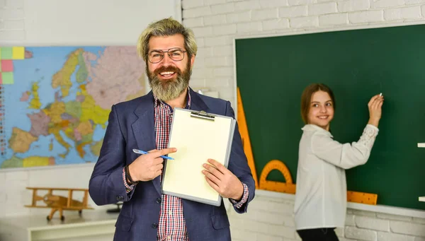 De volta à escola. conceito de educação moderna. professor e criança em sala de aula. alteração de funções. Homem barbudo faz anotações na prancheta. menina escrever resposta no quadro negro. exame ou lição. espaço de cópia — Fotografia de Stock