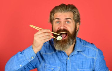 Suşi ruloları. Japon mutfağı. Asya yemeği. Suşi siparişi. Adam evde suşi yiyor. Çubuklu suşi ve zencefil. Doğu kültürü. Sakallı hippi rulo yiyor. Japon yemek servisi.