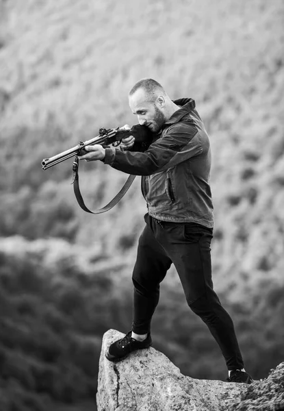 Conceito de caça furtiva. Homem caçador brutal com arma paisagem natural fundo. Caça ilegal. Poacher stand on edge of cliff. Hunter caçador furtivo à procura de vítima. Hunter com rifle ambiente natureza — Fotografia de Stock