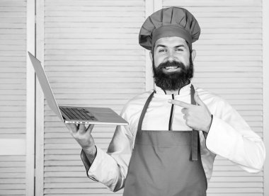 Aşçılık okulu. Şapkalı ve önlüklü hippi internetten ürün alıyor. İnternetten alışveriş. Teslimat servisi. Aşçı adam internette yemek pişiriyor. Market çevrimiçi. Mutfakta şef dizüstü bilgisayar.