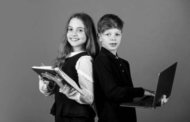 İlkokul öğrencileri. Küçük öğrenciler kitabı ve dizüstü bilgisayarı kahverengi arka planda tutarlar. Okulda küçük öğrenciler okuyor. Zeki öğrenciler ya da okul çocukları. E-öğrenme ve çevrimiçi eğitim. Yeni teknoloji