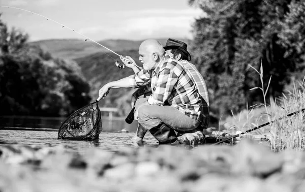 Hermosa noche junto al río. Los hombres río captura de peces. Enseñando pesca. Transfiriendo conocimiento. Los amigos pasan un buen rato a orillas del río. Compartir sus secretos. pescador experimentado mostrar consejos a hijo — Foto de Stock