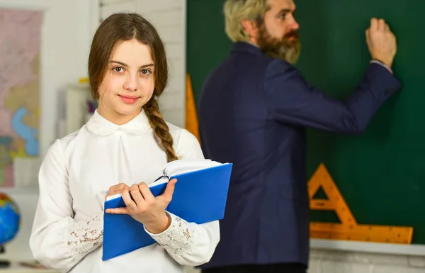 Educazione. piccola ragazza leggere il libro. uomo barbuto scrivere risposta sulla lavagna. esame o lezione. Torniamo a scuola. sviluppo dell'educazione infantile. bambino e insegnante in classe. cambiamento di mansioni. prendere appunti — Foto Stock