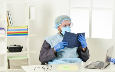 Kendini nasıl koruyacağını öğren. Adam kitap okuyor. Tıbbi araştırma. Koruyucu ekipman işçisi. Doktor çalışıyor. Coronavirüs salgını. En son bilimsel bulgular ve koronavirüs hastalığı hakkında bilgi