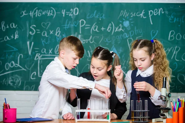 Study of liquid states. Group school pupils with test tubes study chemical liquids. School laboratory. Girls and boy providing experiment with liquids. Test tubes with colorful liquid substances