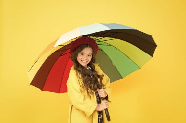 Parlak şemsiye. İyi eğlenceler. Çocuk kız mutlu renkli gökkuşağı şemsiye tutun. Uygun giysiler ile yağmurlu hava. Pozitiflik kavramı. Yağmurlu gün eğlencesi. Şemsiyenin altında mutlu bir yürüyüş. Yağmur konseptinin keyfini çıkarın