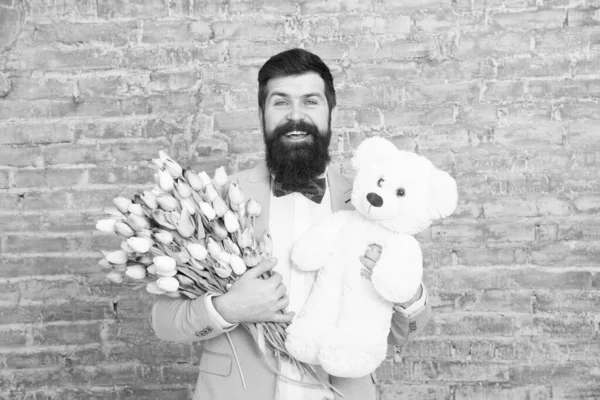 Romantic man. Macho getting ready romantic date. Waiting for darling. Man well groomed wear tuxedo bow tie hold flowers tulips bouquet and big teddy bear toy. Invite her dating. Romantic gift