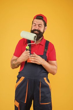 Boya aletini tamir et. Patenli neşeli sakallı işçi. Hipster sanatçı dekoratörü sarı duvar. İş üniformalı ereksiyon asistanı. Mühendis tasarımcı duvarı boyamaya hazır. onarım kavramı