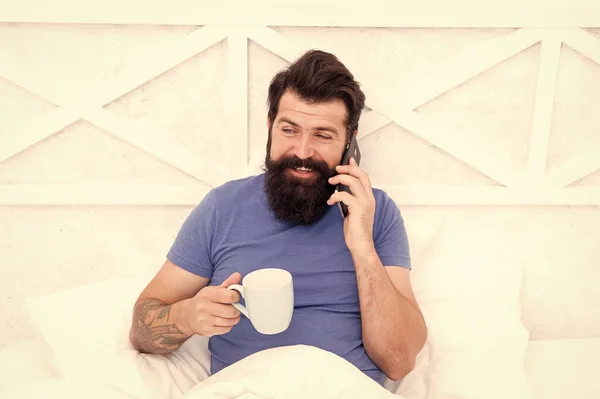 你好，亲爱的 留胡子的男人在床上使用移动技术。 帅哥在电话里聊天，在家里喝咖啡。 现代生活新技术。 技术概念。 愉快的谈话。 1.早上好 — 图库照片