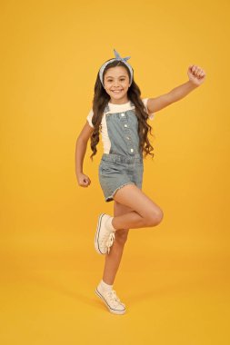 İçinde enerji var. Tatil zamanı. Moda modası. Biraz modacı sarı arka plan. Sevimli çocuk moda kızı. Yaz moda konsepti. Uzun kıvırcık saçlı, başörtülü bir kız. Saç bakımı. Etkin yaşam biçimi