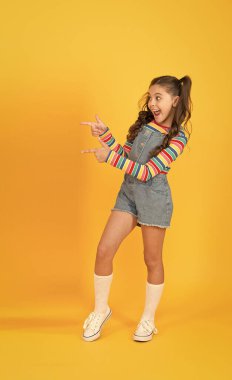 Mutlu çocukluk. Retro kız yaz tatilinin tadını çıkarıyor. Küçük sarı arka plan. Okul alışveriş pazarı. Kaygısız ve komik çocuk. Küçük güzel, uzun saçlı. Kaliteli liseli kız işaret ediyor.