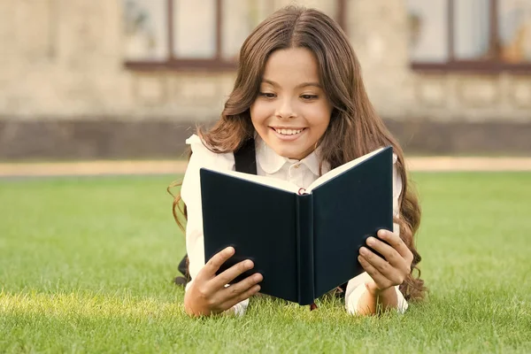 Кто нуждается в отдыхе, когда есть еще одна книга для чтения. Очаровательный маленький ребенок читает книгу о зеленой траве. Милая маленькая девочка расслабляется чтение книги на открытом воздухе. Лови каждый день с новой книгой. Школа и знания — стоковое фото