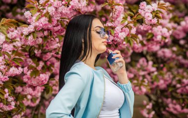 Kiraz çiçeği aroması. Kadın parfümü. Bahar parfümü. Süslü bir tarz. Aromatik bileşikler. Doğal kokulu gerekli yağlar. Eau de Toilette 'de. Şatafatlı bir koku. Modaya uygun bir kadın parfüm şişesi tutuyor.