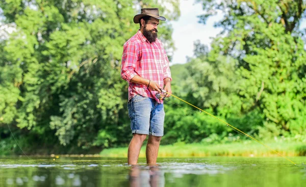 Una meditación amable. Peces normalmente capturados en estado salvaje. Granja de truchas. Pescador solo de pie en el agua del río. Hombre pescador barbudo. Equipo de pesca del pescador. Actividad deportiva Hobby. Humor tranquilo y pacífico — Foto de Stock