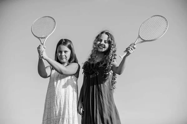 Vida activa. Los niños juegan tenis azul cielo fondo. Niños deportistas. Chicas pequeñas con raqueta de tenis rosa. Ocio de verano. Juego de deportes. Niños alegres juguetones. Feliz infancia. Positivo. Equipo de chicas — Foto de Stock