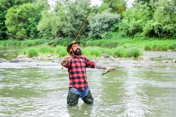 Visser mannelijke hobby. Visserijuitrusting. Vis aan haak. Brutale man draagt rubberen laarzen staan in rivierwater. Tevreden visser. Vissen vereist dat je bewust en volledig aanwezig bent in het moment — Stockfoto