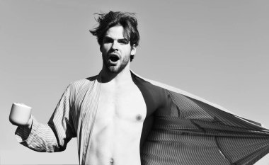 Mavi çizgili pijamalı, elinde fincanla beyaz maço.