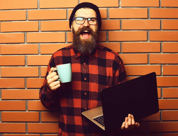 Brutalny, biały hipster trzymający laptopa z kubkiem — Zdjęcie stockowe