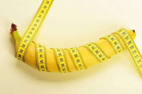 Centimeter ruler spinned around fresh fruit. Yellow tape around banana isolated on white background.