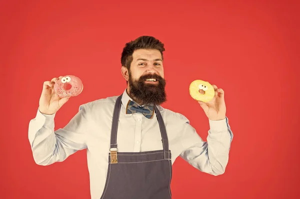 Glucides et calories. Barbu gai homme bien soigné vendant des beignets. Propriétaire de boulangerie. Boulangerie. Des pâtisseries. Bonbons et gâteaux. De la malbouffe. Hipster boulanger barbu manger des beignets. Boulangerie de beignets — Photo