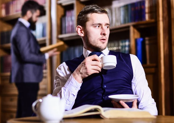 British elite or aristocrats spend leisure in library, drink tea.