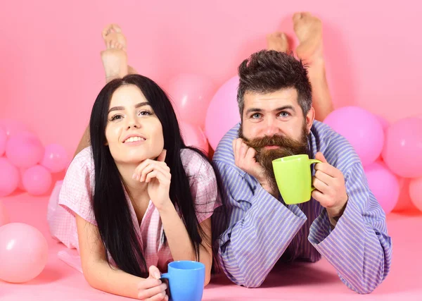 Odpočiňte si ráno u kávy. Muž a žena na usměvavých tvářích leželi na růžovém pozadí. Víkendový ranní koncept. Muž a žena v domácích šatech, pyžamo. Pár v lásce pít kávu v posteli. — Stock fotografie
