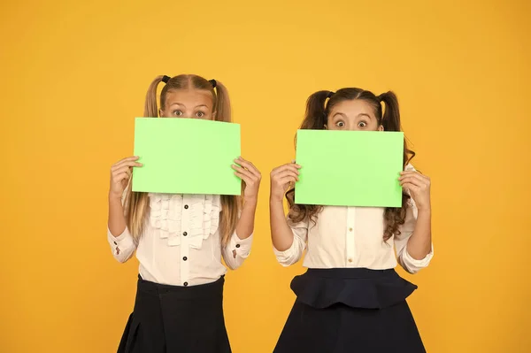 No proszę. Dziewczynki trzymające puste kartki papieru na żółtym tle. Małe dzieci z pustym zielonym papierem szkolnym do zadań lub prac projektowych. Papiery egzaminacyjne. Papier akademicki, przestrzeń do kopiowania — Zdjęcie stockowe
