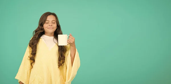 귀여운 아가씨가 커피를 들고 있네. 좋은 아침 음료. 작은 파란 벽. 어린 소녀는 잠들기 전에 코코아 우유를 마신다. 아늑하고 푹신 한 파자마. 편안 함을 느끼는 거죠. 복사 공간. 찻잔에 담긴 행복 한 소녀 — 스톡 사진
