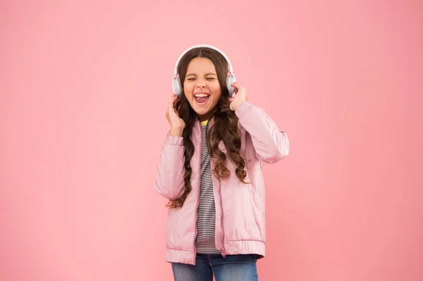 full of emotions. Little child do vocal on song. Emotional singer. Enjoying song playing in headphones. Karaoke and entertainment. Joining in a song. Small girl sing to song pink background