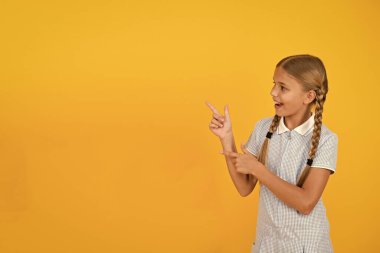 Şuna bak. Mutlu küçük okul kızı sarı arka plan kopyalama alanı parmak işaret. Okula geri dön. Dikkat kavramı. Reklam modeli. Okul ürünü sunan schoolgirl. Pozitif çocuk