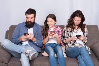 Aile eğlencesi. Oyun uygulaması oynat. Çevrimiçi aile. Aile hafta sonunu internette geçiriyor. Küçük bir kız çocuğu, ailesine karşı akıllı telefon kullanıyor. İnternette aile sörfü. Anne baba ve kızı kanepede dinleniyor.