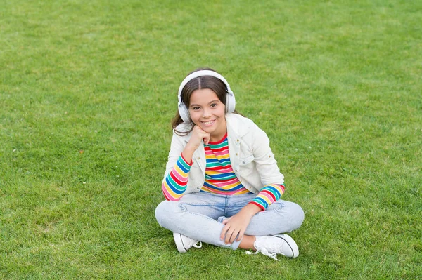 起こるようにしなさい。屋外でリラックスしながら音楽を聴く。子供の女の子は音楽の緑の草の牧草地を楽しむ。楽しい時間だ。子供のヘッドフォンは音楽を聞く。クールな女の子のヘッドフォン音楽を聞いて。教育ポッドキャスト — ストック写真