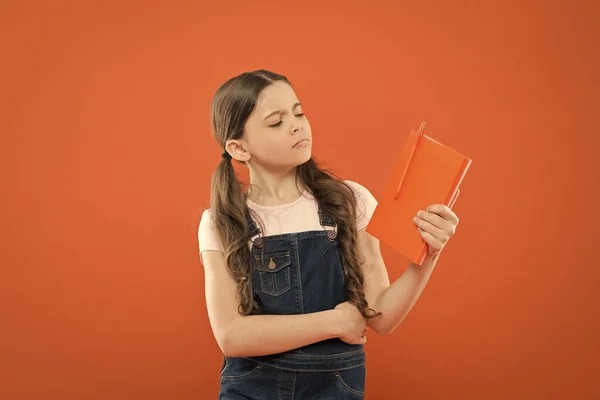 Waar gaat dit boek over? literatuur les. terug naar school. schoolmeisje lezen boek op oranje achtergrond. poëzie en roman. modern onderwijs. notities schrijven. Kid Diary. denken klein meisje met notebook — Stockfoto