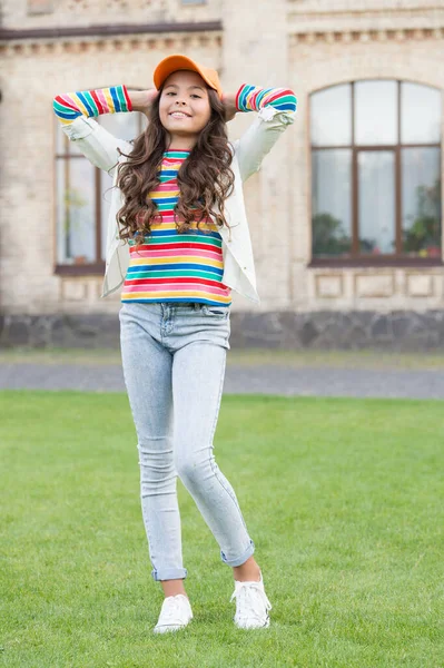 Niño morena bonita en la calle. moda de primavera y belleza. Feliz día de los niños. niño con estilo en la tapa. sonrisa cálida y amigable. concepto de estilo de vida saludable. linda niña tiene el pelo rizado —  Fotos de Stock