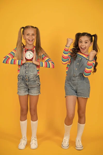 Deux filles heureuses tiennent le réveil. retour à l'école. l'été. discipline et gestion du temps. adolescent filles mur jaune. horloge vintage pour enfants. compter pour l'heure du déjeuner. concept de rupture enfants — Photo