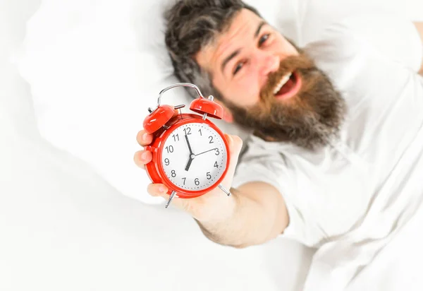 Egy boldog arcú férfi fekszik a párnán, tartja az ébresztőórát.. — Stock Fotó