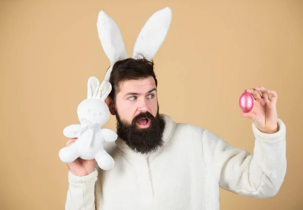 Easter rabbit. Man wearing rabbit suit. Funny bunny man soft ears. Easter activities concept. Weirdo concept. Celebrate Easter. Guy bearded hipster weird bunny with long white ears beige background