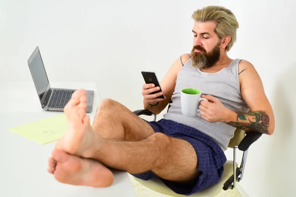 Multitasking. relaxed man sit on comfortable chair using laptop. online in social media. working barefoot at home office. social distancing concept. man is working at home during coronavirus pandemic